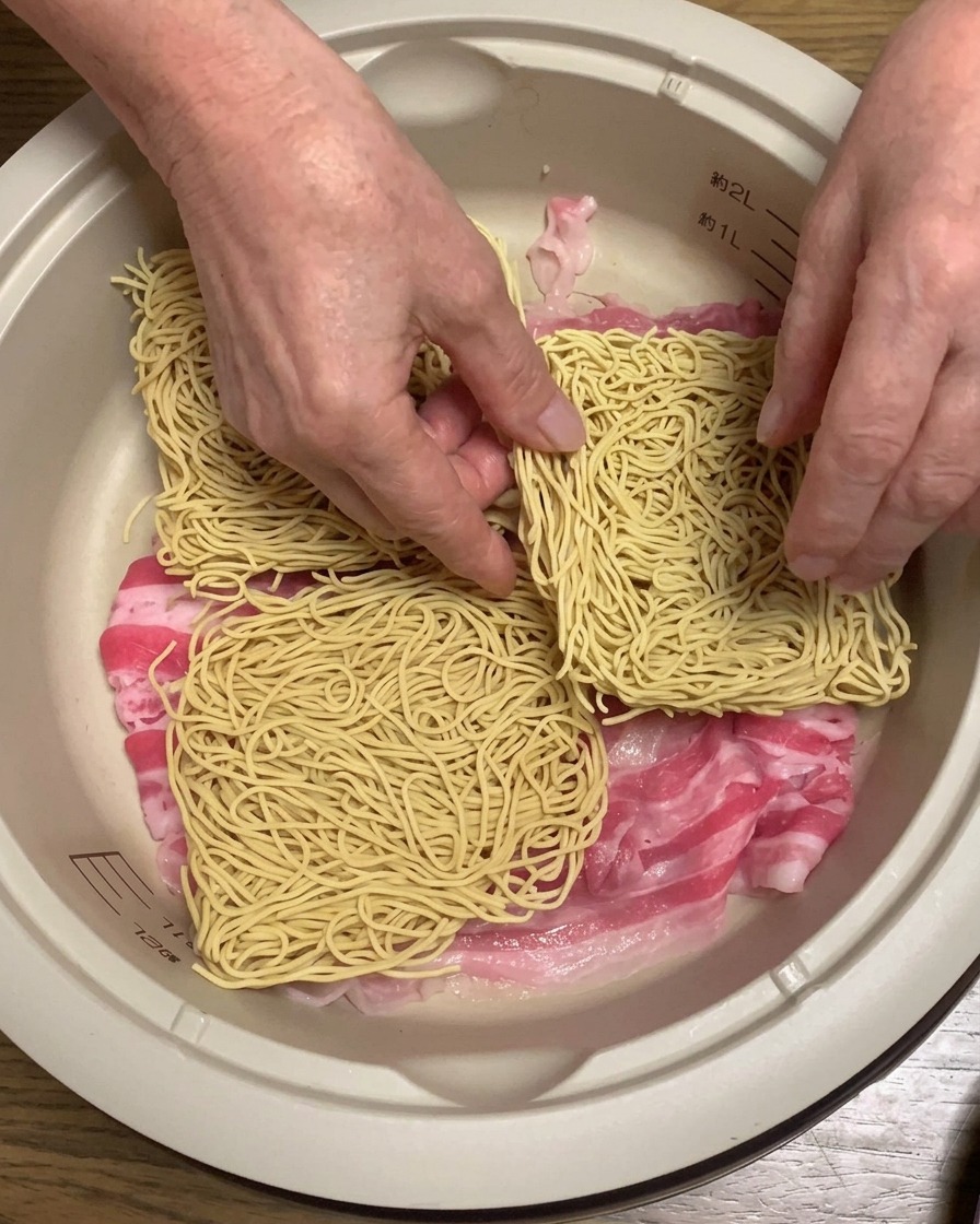 豚バラ肉の上に乾燥したラーメンの麺をのせている様子。