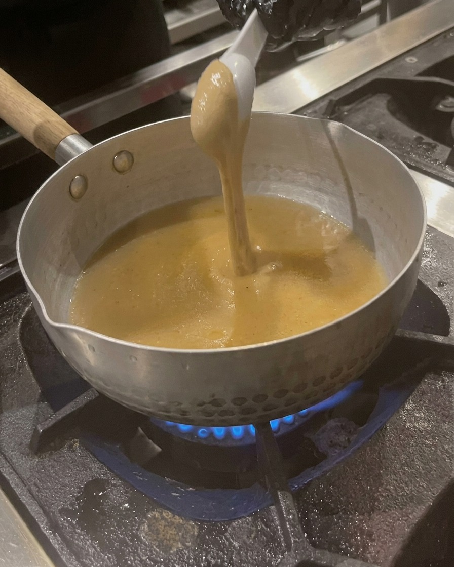小鍋で温まるスープに、スプーンで練りごまを溶かし入れている様子。
