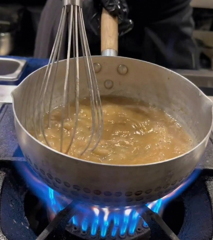 沸騰したお湯の中で、網を使ってラーメンの麺を茹でている様子。