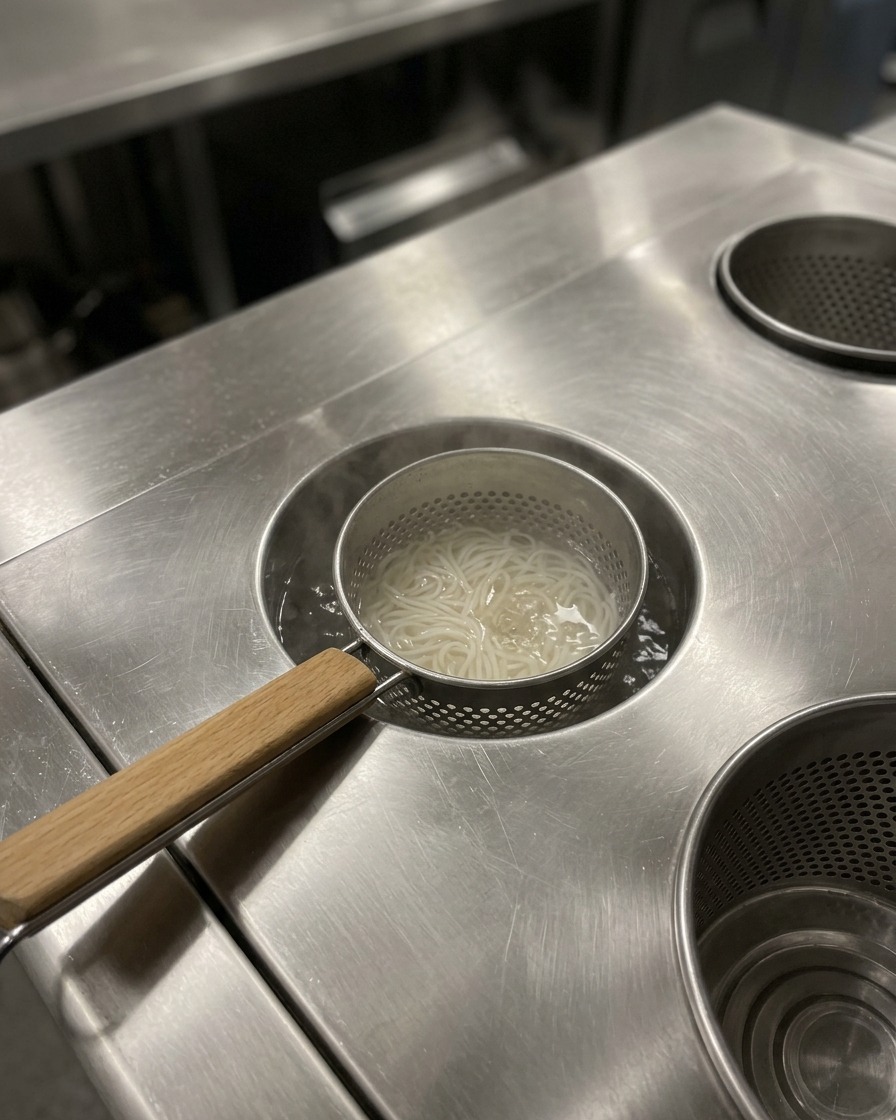 丼に入った茹でたての麺に、熱々のスープを注ぐ準備をしている様子。