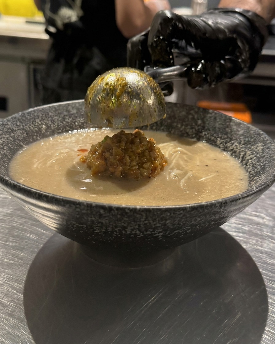 ラーメンの表面に、スプーンでラー油を円を描くように回しかけている様子。