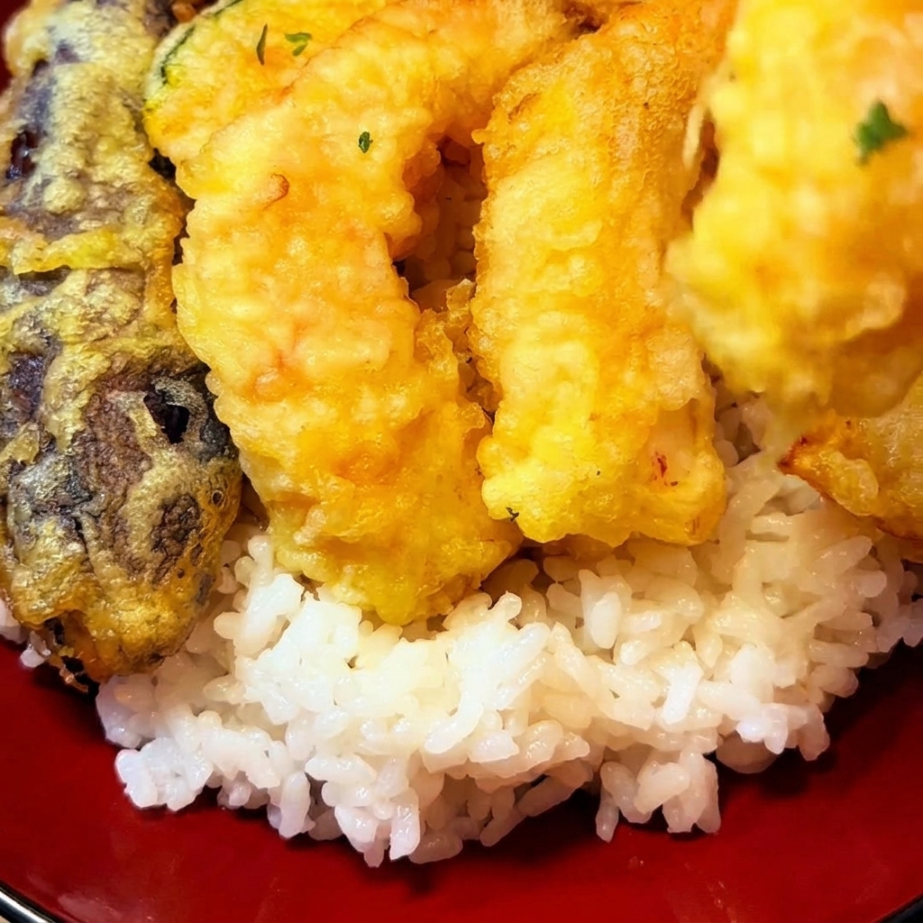 揚げたての天ぷらを丼ご飯の上に美しく盛り付けている様子。