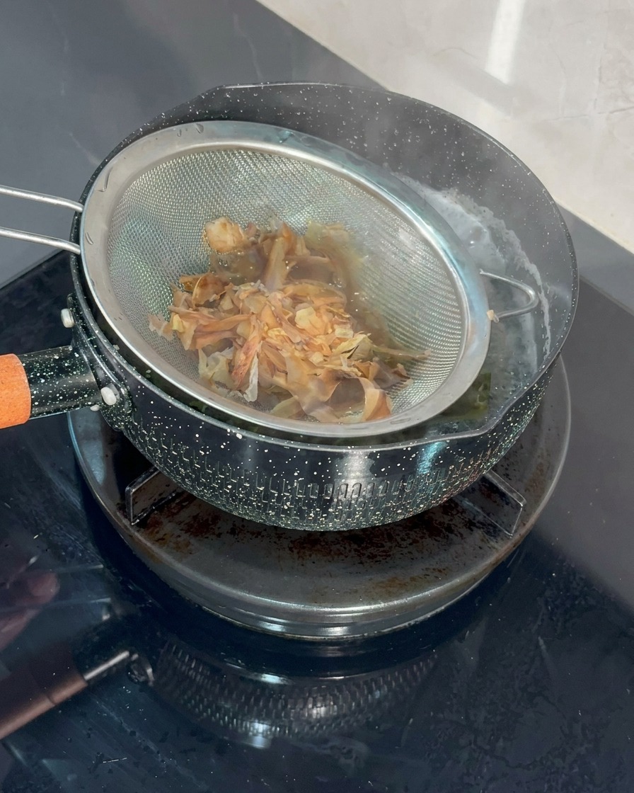 細かい網のストレーナーで鰹節を熱湯にくぐらせている様子。