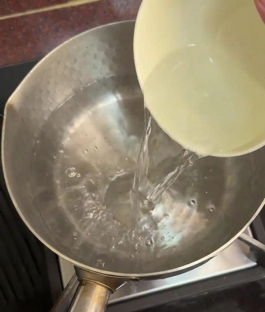 コンロの上のステンレス鍋に入った熱湯に、セラミックのボウルから透明な冷水を注ぎ入れている様子。