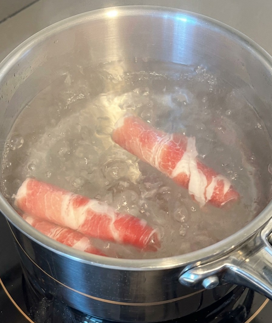 沸騰したステンレスの鍋に、生の牛バラ薄切り肉を2巻きほど入れて茹でている様子。