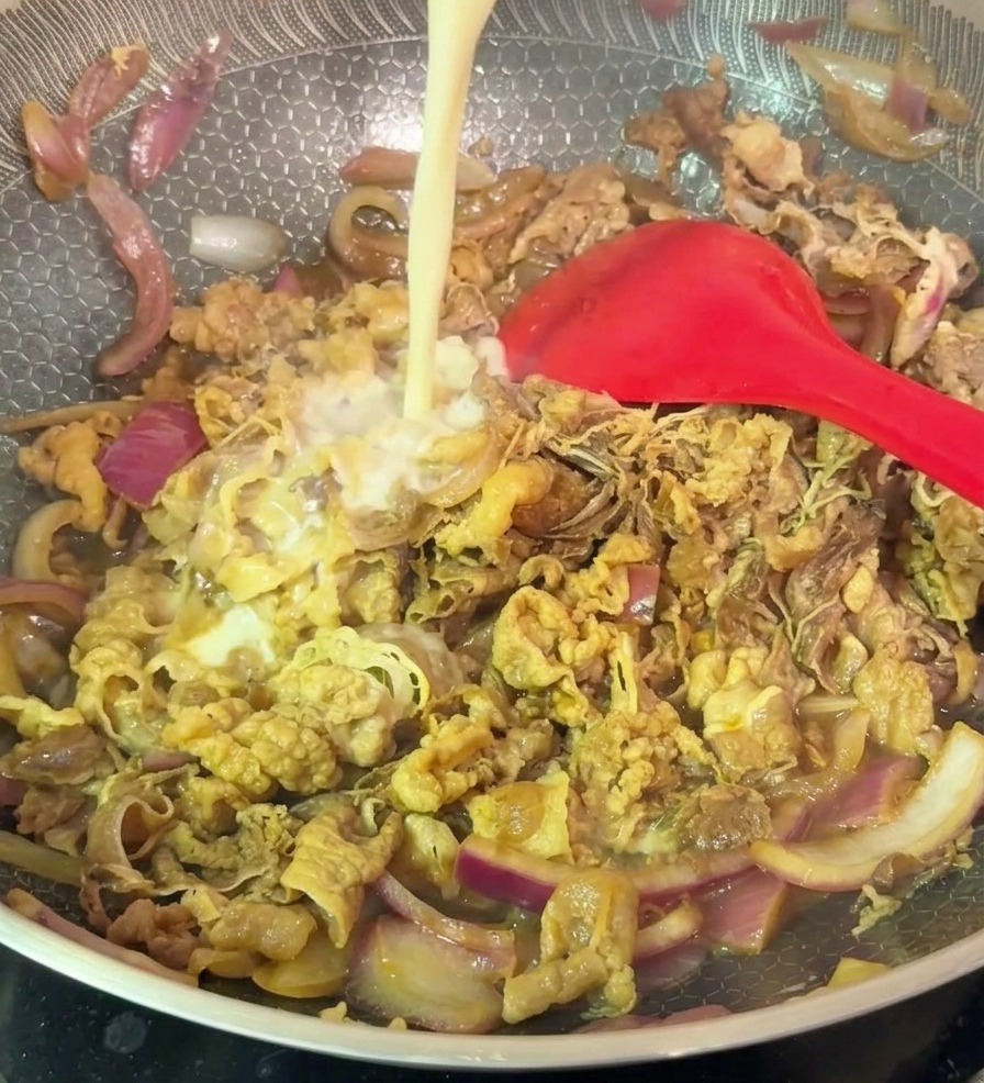 ハニカム模様のフライパンに入った牛肉と赤玉ねぎの炒め物に、白い水溶き片栗粉を少しずつ回し入れている様子。