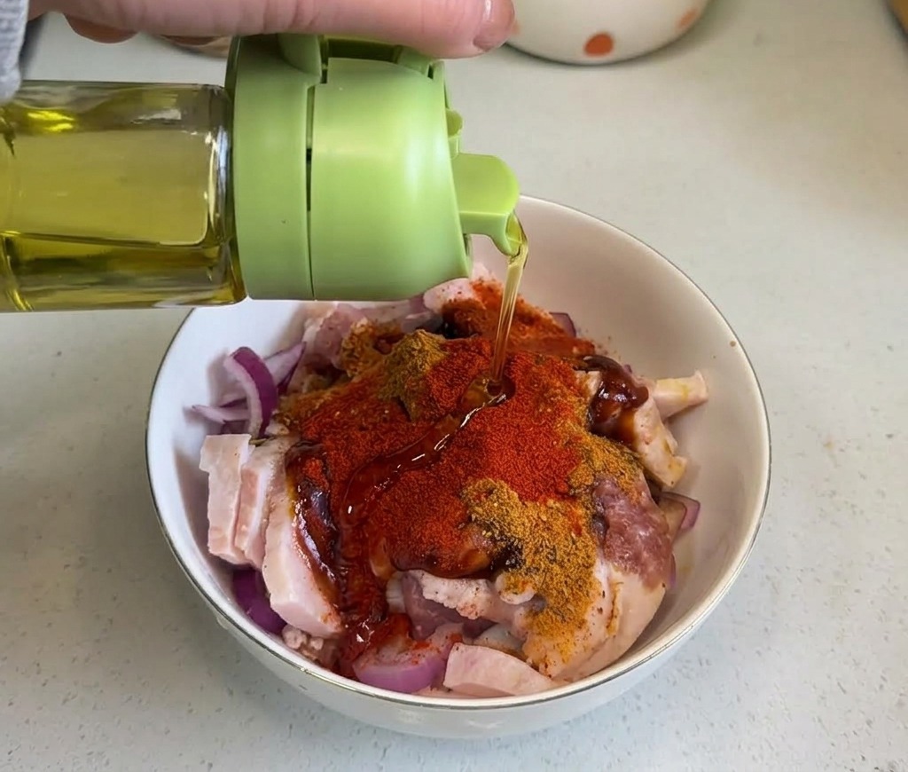 スパイスで味付けされた豚バラ肉のミクスチャーに、緑色のボトルから透明なサラダ油を回し入れている様子。