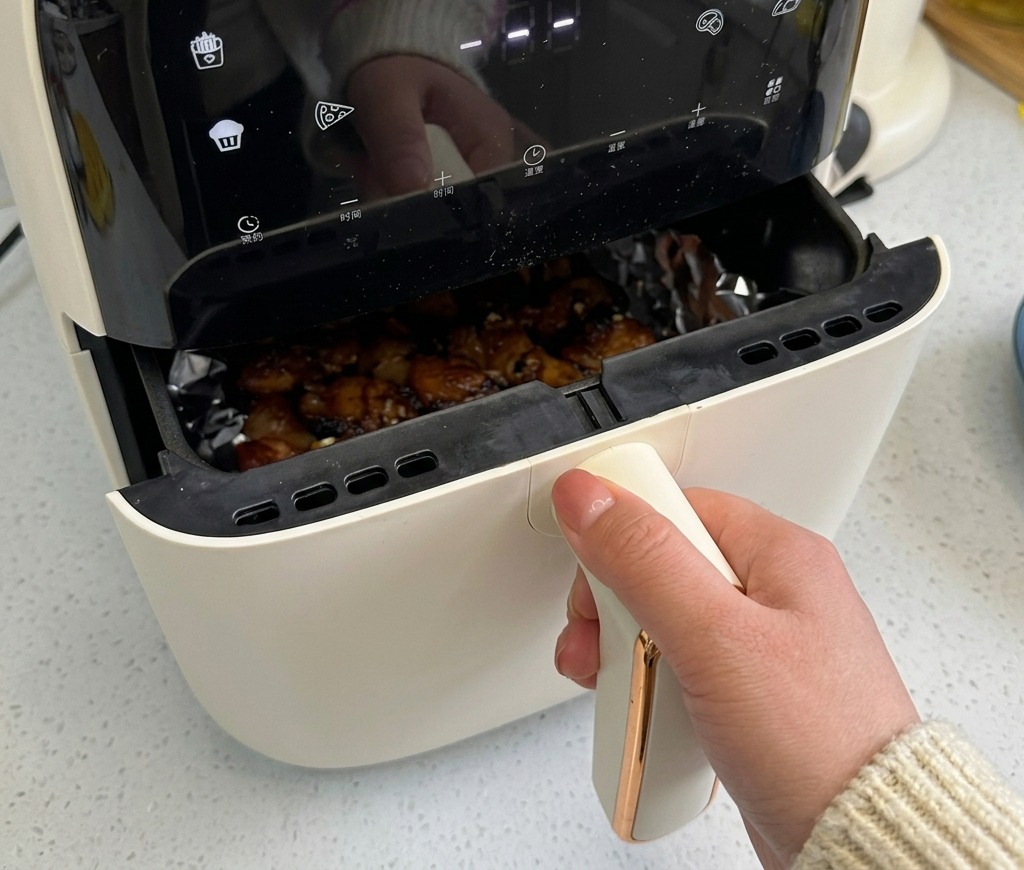 ノンフライヤーのバスケットが半分引き出され、中にある豚バラ肉が茶色く色づき、ジューシーに音を立てて焼けている様子。
