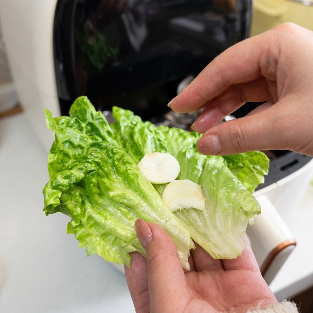 緑色のレタスの葉の上に、新鮮な白い生にんにくのスライスを2枚のせている手の接写。