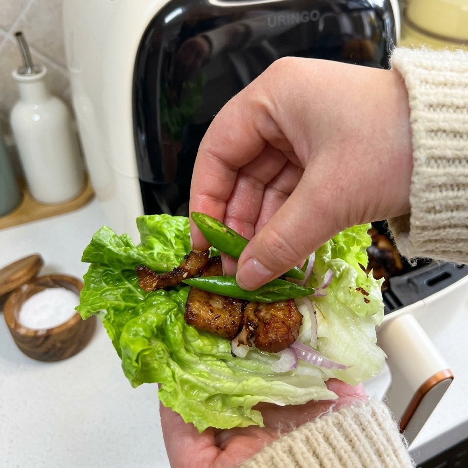 カリカリの豚バラ肉と玉ねぎが入ったレタス包みの上に、小さな鮮やかな緑色の青唐辛子を2つ添えている手の様子。