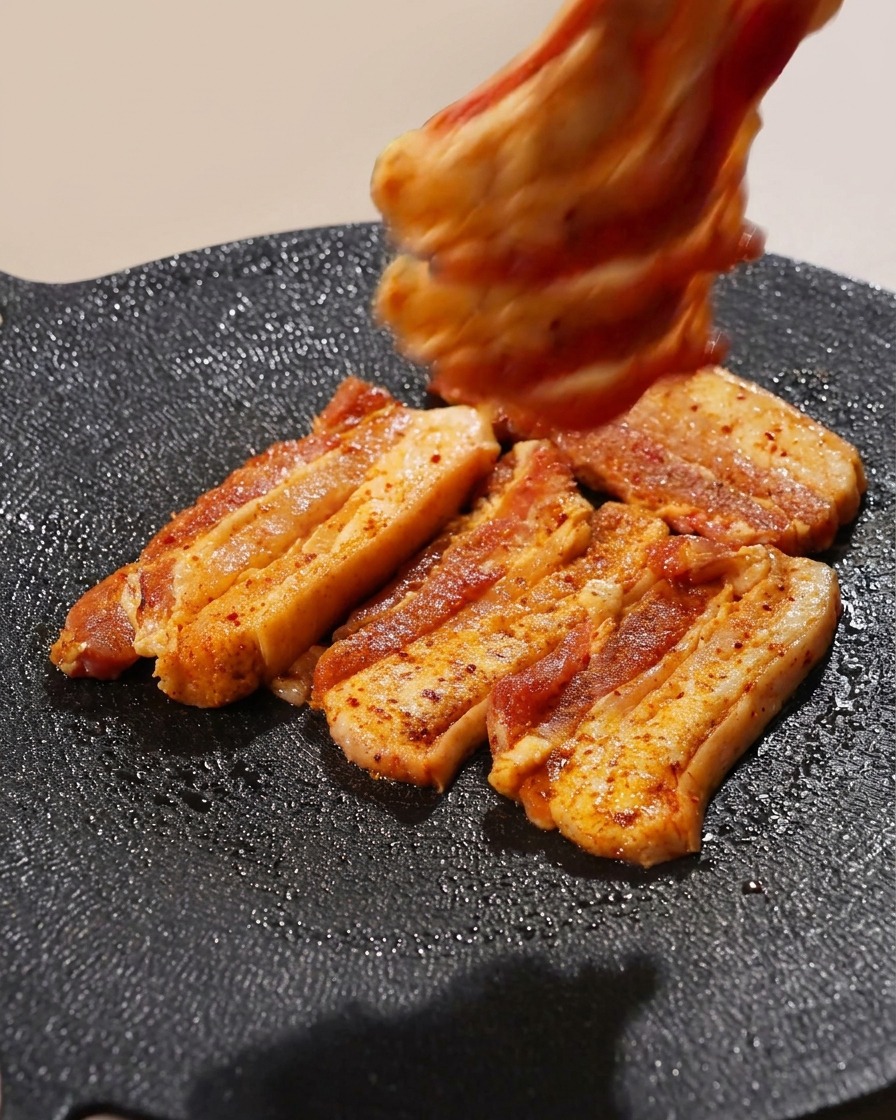 熱いグリルパンの上に、味付けした豚バラ肉をきれいに並べている様子。