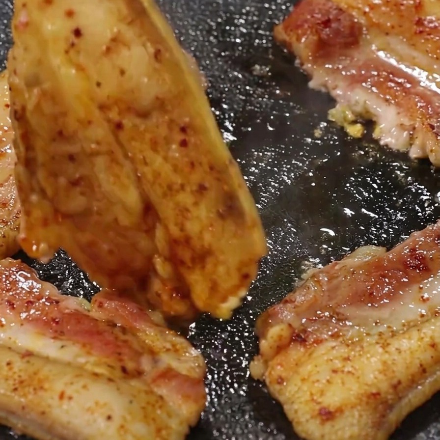 トングを使って、きつね色に焼け始めた豚バラ肉をひっくり返している様子。