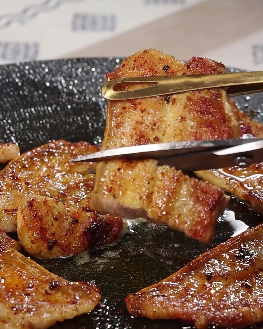 トングで持ち上げた焼き立ての豚バラ肉を、キッチンバサミでカットしている様子。