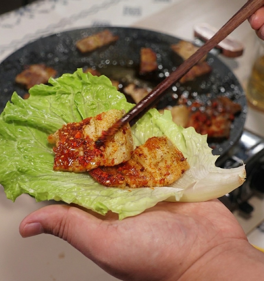 手のひらに広げた大きなサンチュの葉に、お箸でお肉をのせている様子。