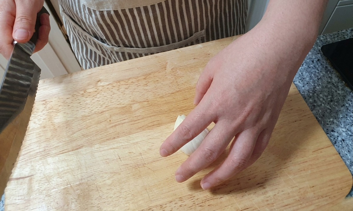 木製のまな板の上で、包丁を使って白い玉ねぎを薄く均一にスライスしている様子