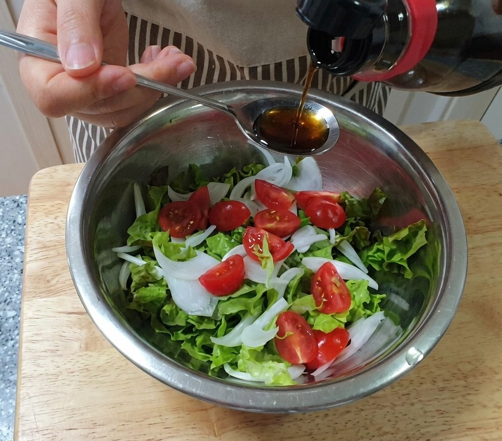 レタス、玉ねぎ、ミニトマトが入ったボウルに、スプーンから手作りドレッシングを回しかけている様子
