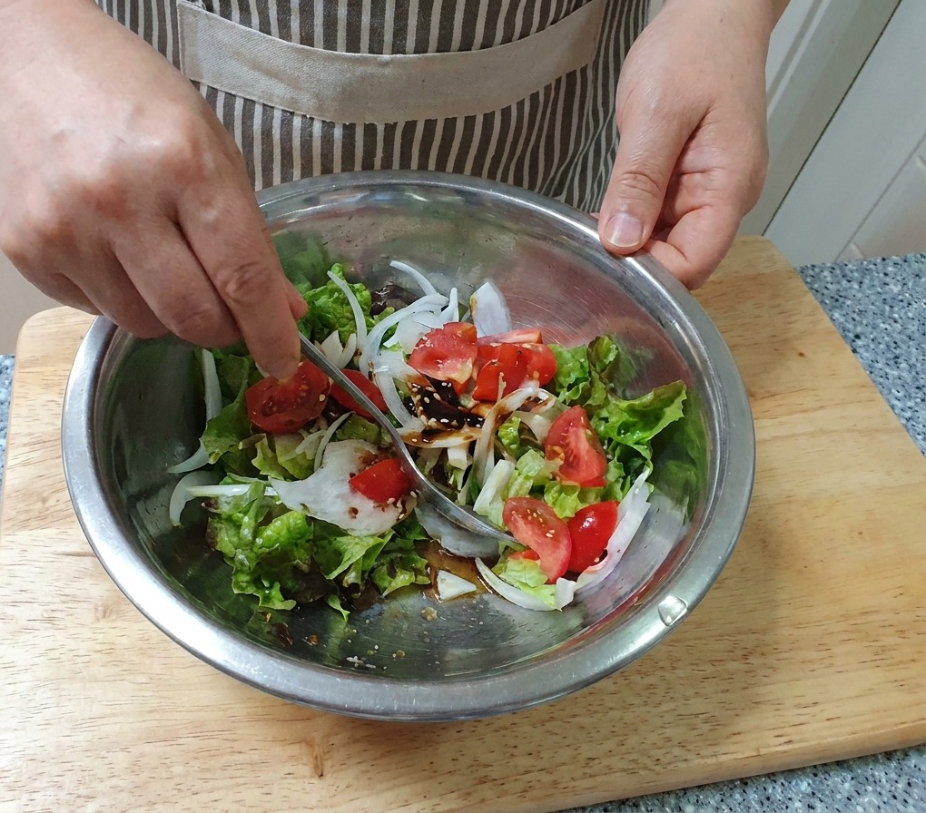 大きめのステンレス製ボウルの中で、手を使って新鮮な野菜サラダをスプーンでふんわりと混ぜ合わせている様子