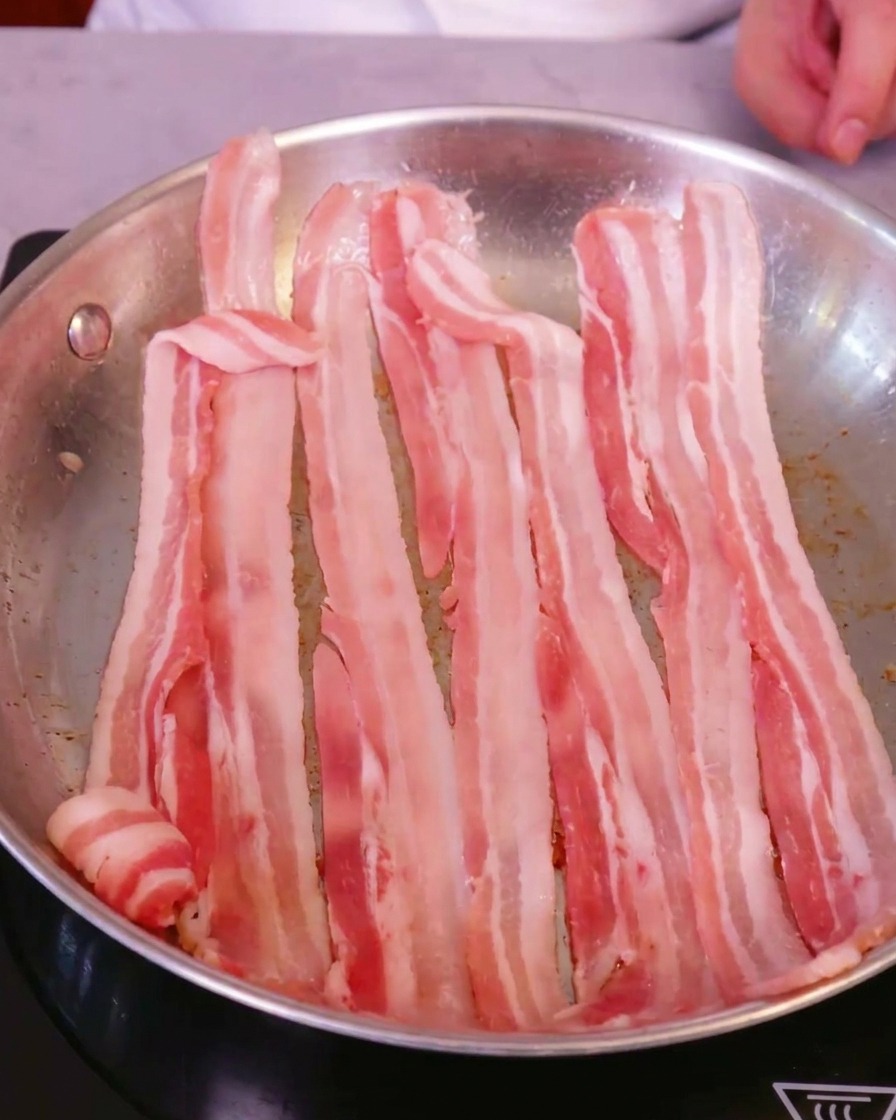 IHクッキングヒーターの上の大きなステンレス製フライパンに、きれいに並べられた生の豚バラ肉のスライス。