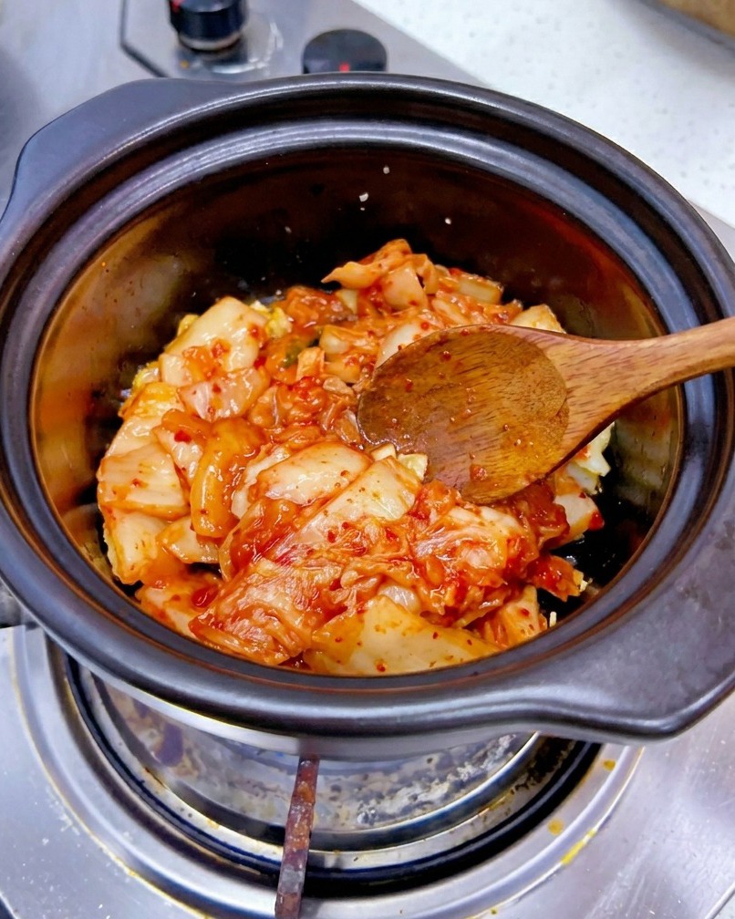 炒めたにんにくとオイルが入った鍋に、刻んだ白菜キムチを加えている様子。