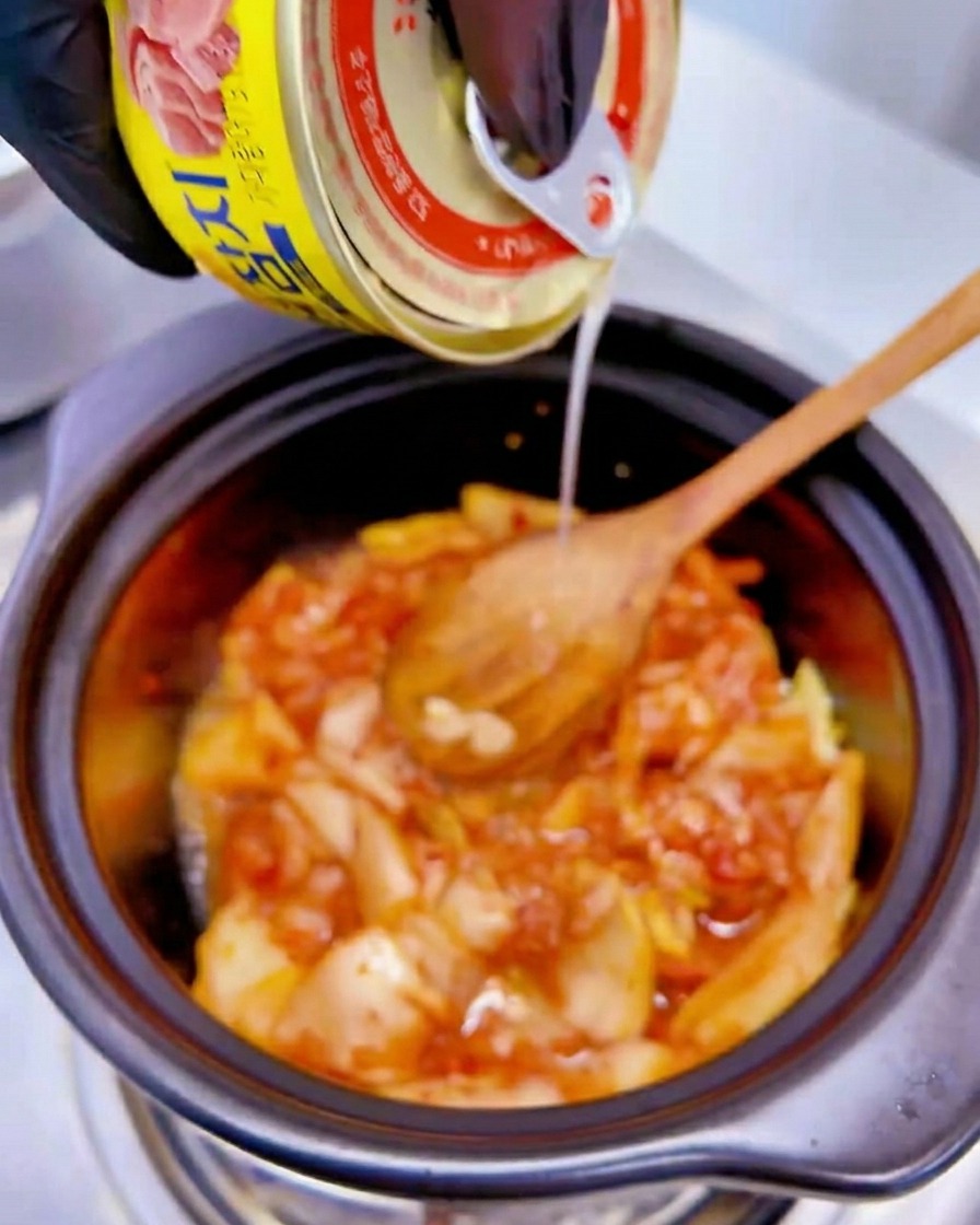 鍋のキムチに、黄色いツナ缶から汁が注がれている様子。