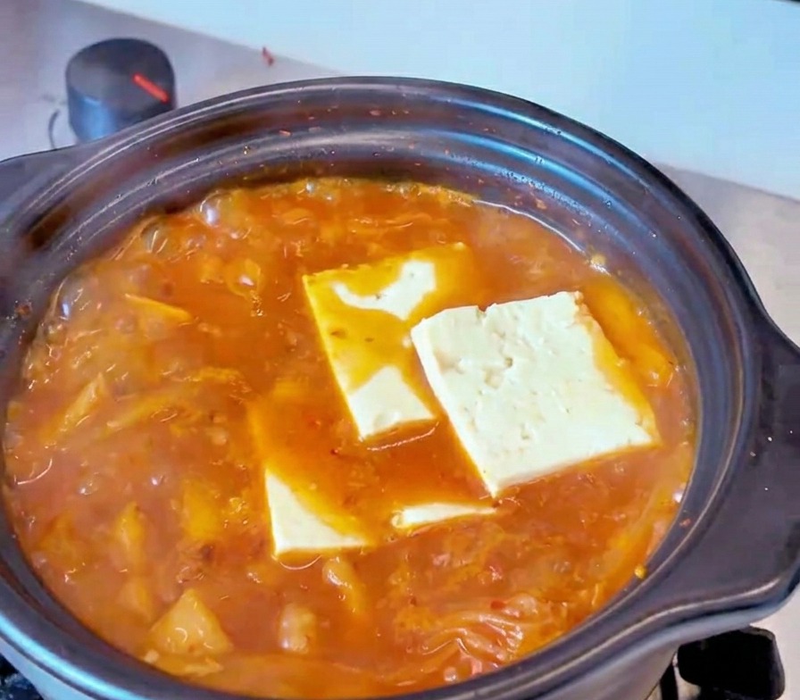 グツグツと沸騰する赤いキムチチゲのスープの中に、長方形にカットされた白い豆腐が並べられている様子。