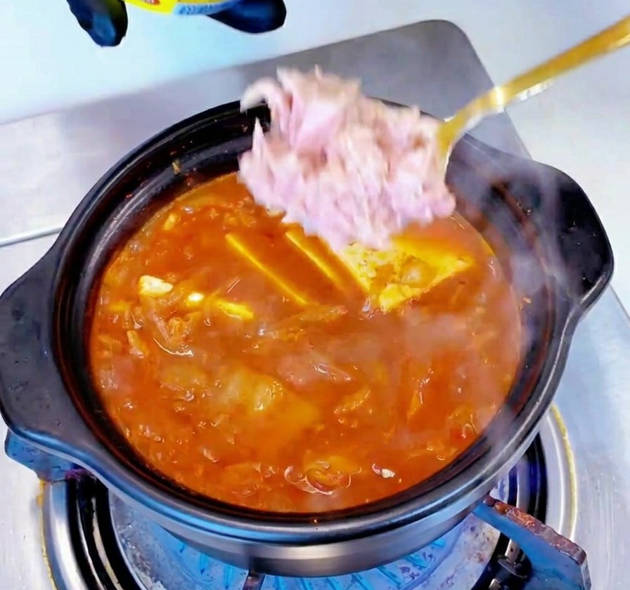 グツグツと煮立つ赤いスープの中央に、ライトピンクのツナの塊をスプーンで入れている様子。