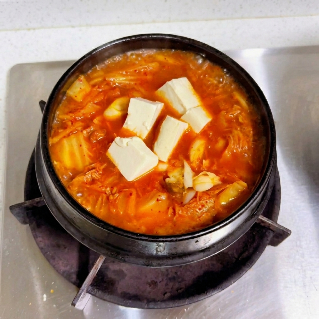 黒い鍋の中の沸騰する赤いキムチスープの上で、白い木綿豆腐がきれいに並んでいる様子。