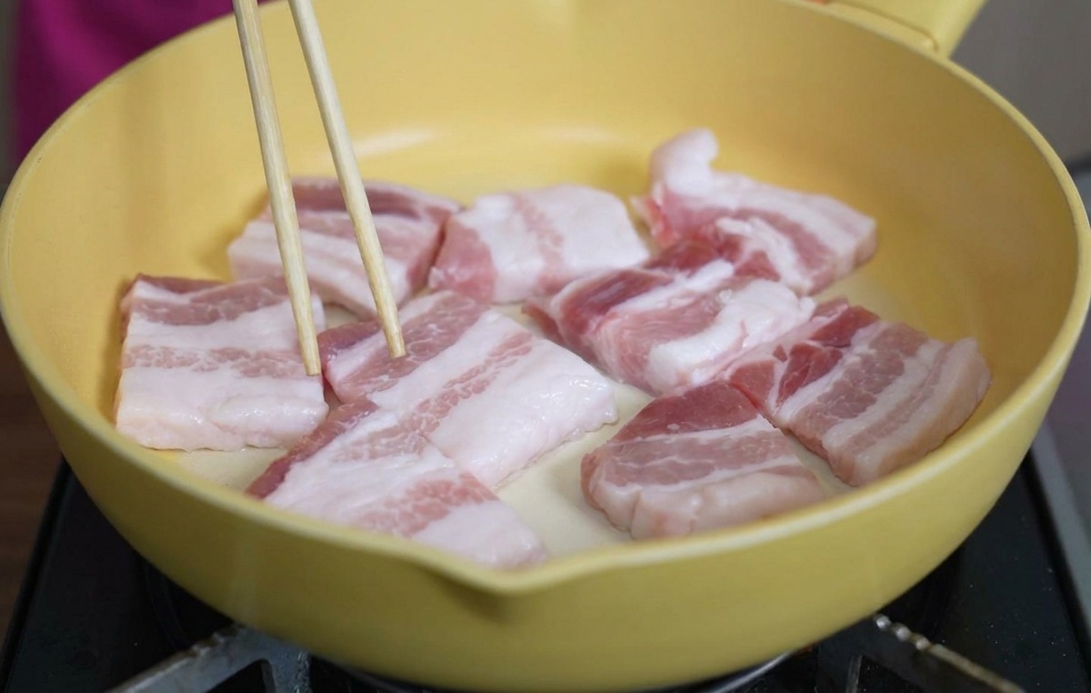 黄色いセラミックフライパンに並べられた厚切りの豚バラ肉を箸で整えている様子