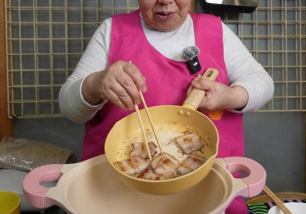 こんがりと焼けた豚バラ肉を、箸を使って黄色いフライパンから大きめのピンクの鍋へ移している様子
