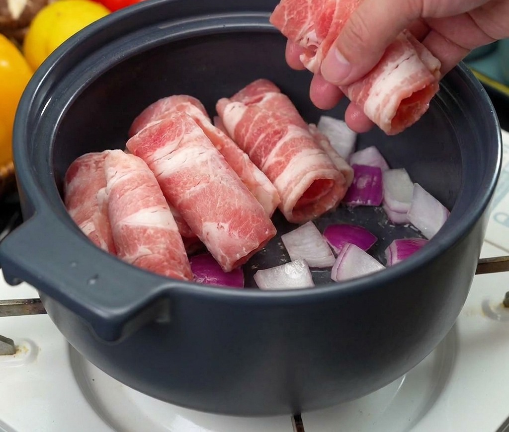 炒めた玉ねぎが入った鍋の中に、薄切りにした生の牛肉を数枚ずつ入れている様子。