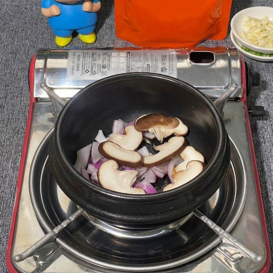 黒い土鍋の中で、紫玉ねぎの上にスライスしたしいたけとほぐしたブナシメジを重ねている様子。