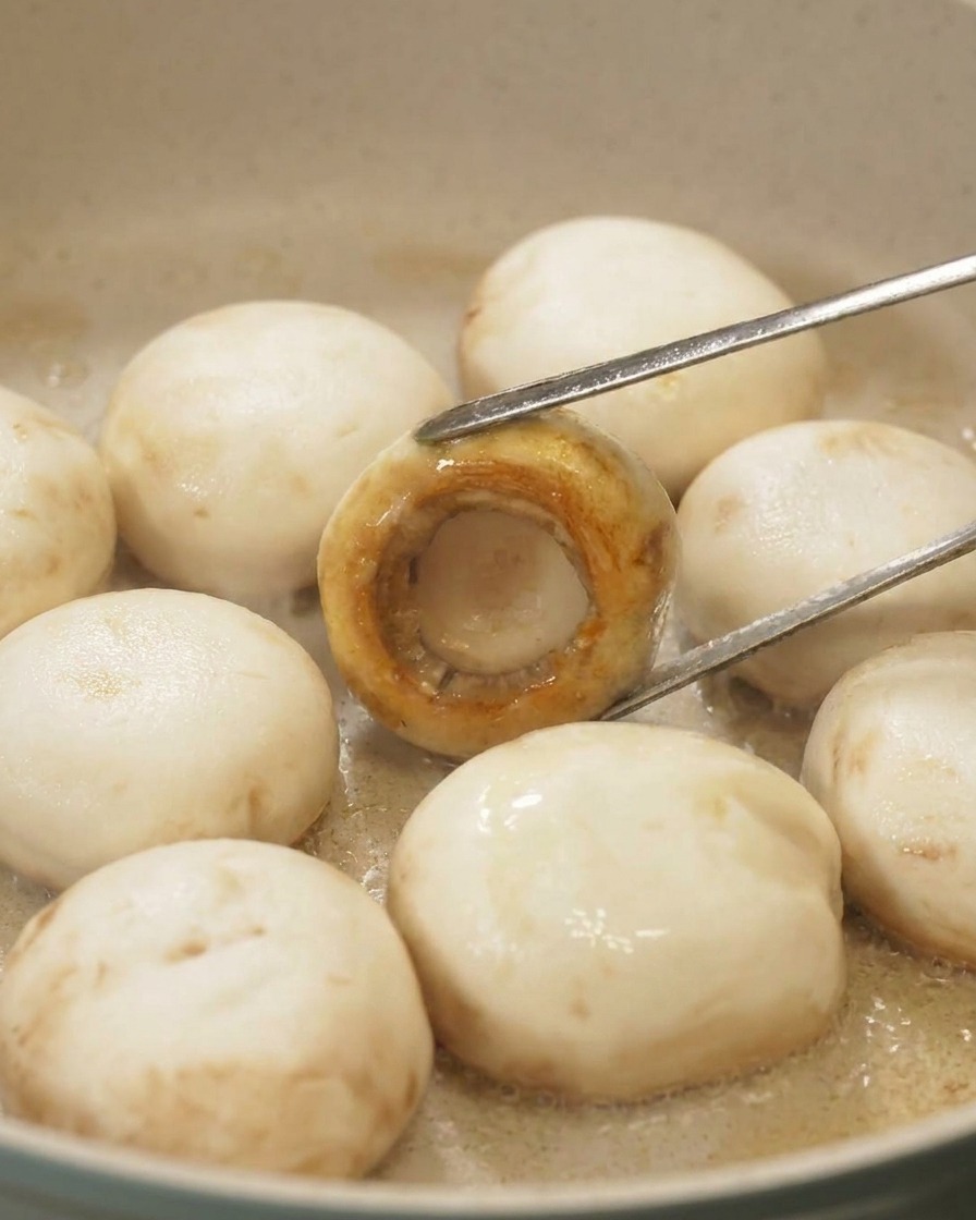 トングでマッシュルームをひっくり返し、かさの表面が均一に香ばしい黄金色に焼き上がっている様子
