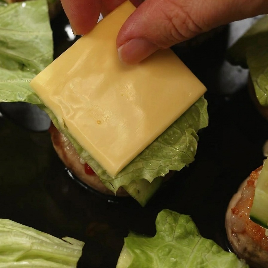 バーガーの中のレタスときゅうりの上に、四角く切った黄色いチーズをのせている手元