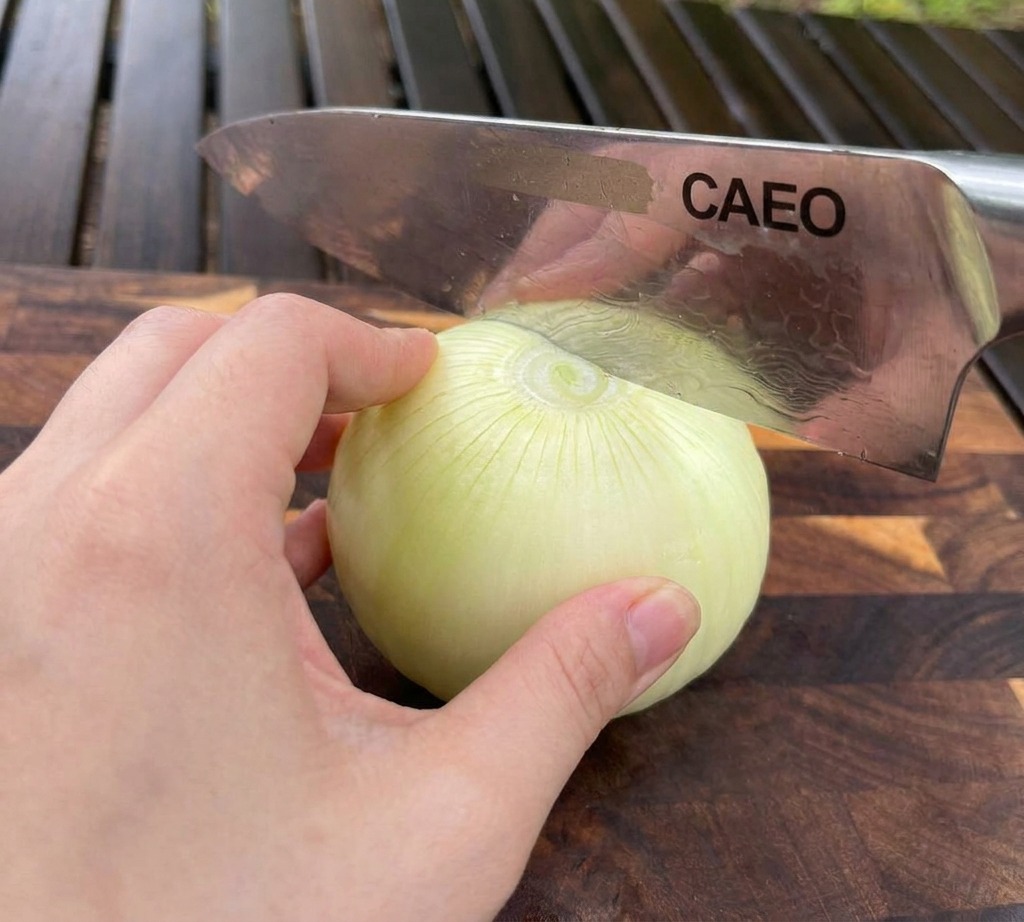 木製カッティングボードの上で白玉ねぎを片手で固定し、牛刀で上から薄くスライスしている手元。