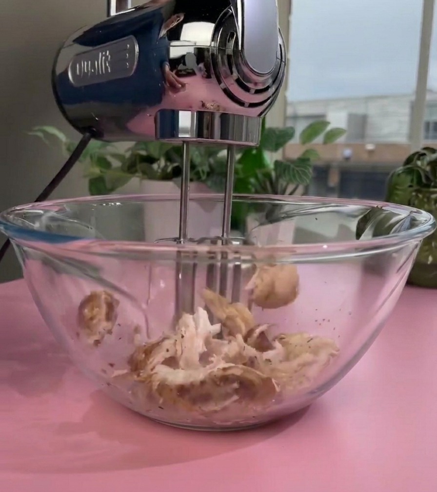 ガラスボウルの中で電動ハンドミキサーを使って調理済みの鶏肉を細かくほぐしている様子。
