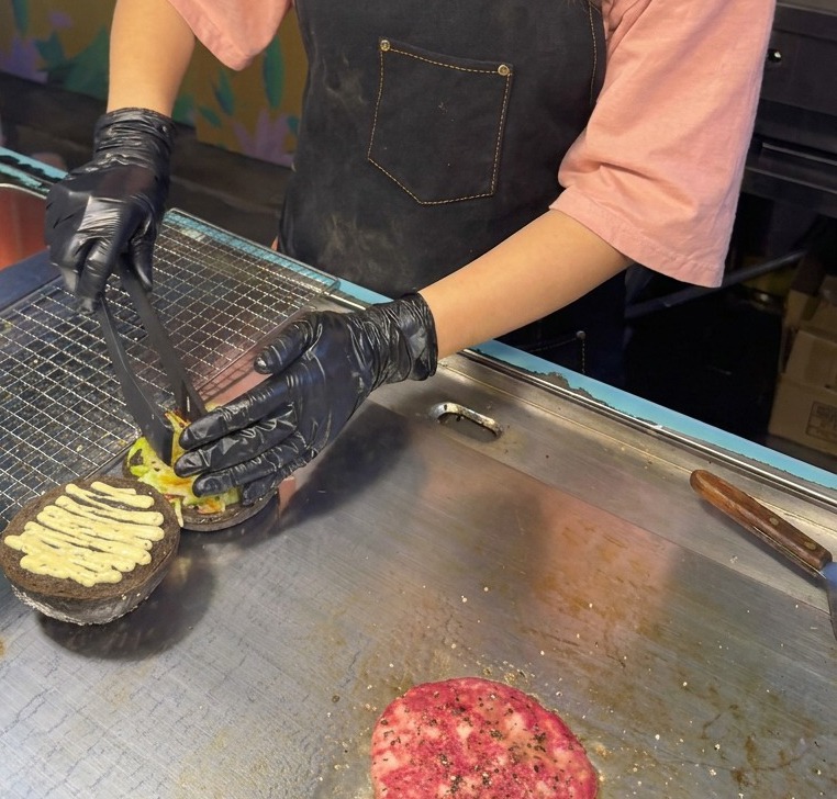 トリュフソースを塗った黒いバンズの上に、トングを使って刻んだレタスと紫キャベツをこんもりとのせている様子。