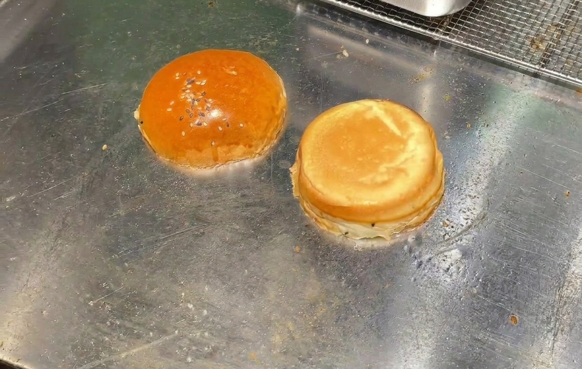 熱い鉄板の上で、半分に切ったバーガー用バンズの断面を下にしてトーストしている様子。