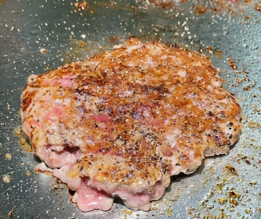 グリル上でひっくり返された牛肉パティの表面が、深くカリッと香ばしい茶色に焼き上がっている様子。