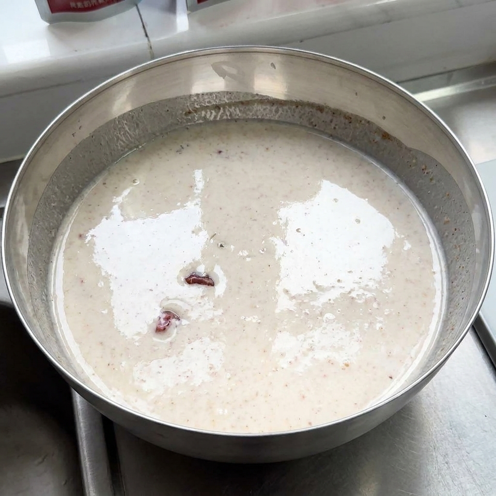 スパイシーでクリーミーなヨーグルトマリネ液で満たされた大きな金属製ボウルに、生の鶏肉が漬かっている様子