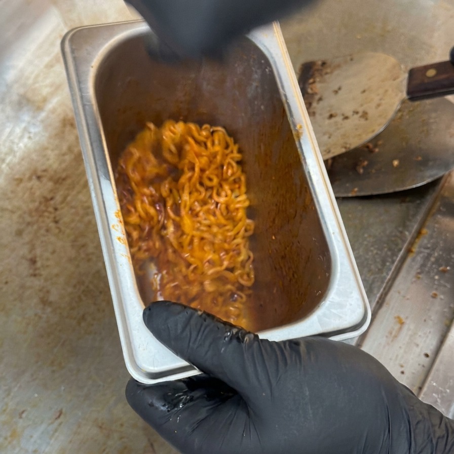 深さのあるステンレス製の容器の中で、真っ赤な激辛麺がしっかりと混ぜ合わされている様子