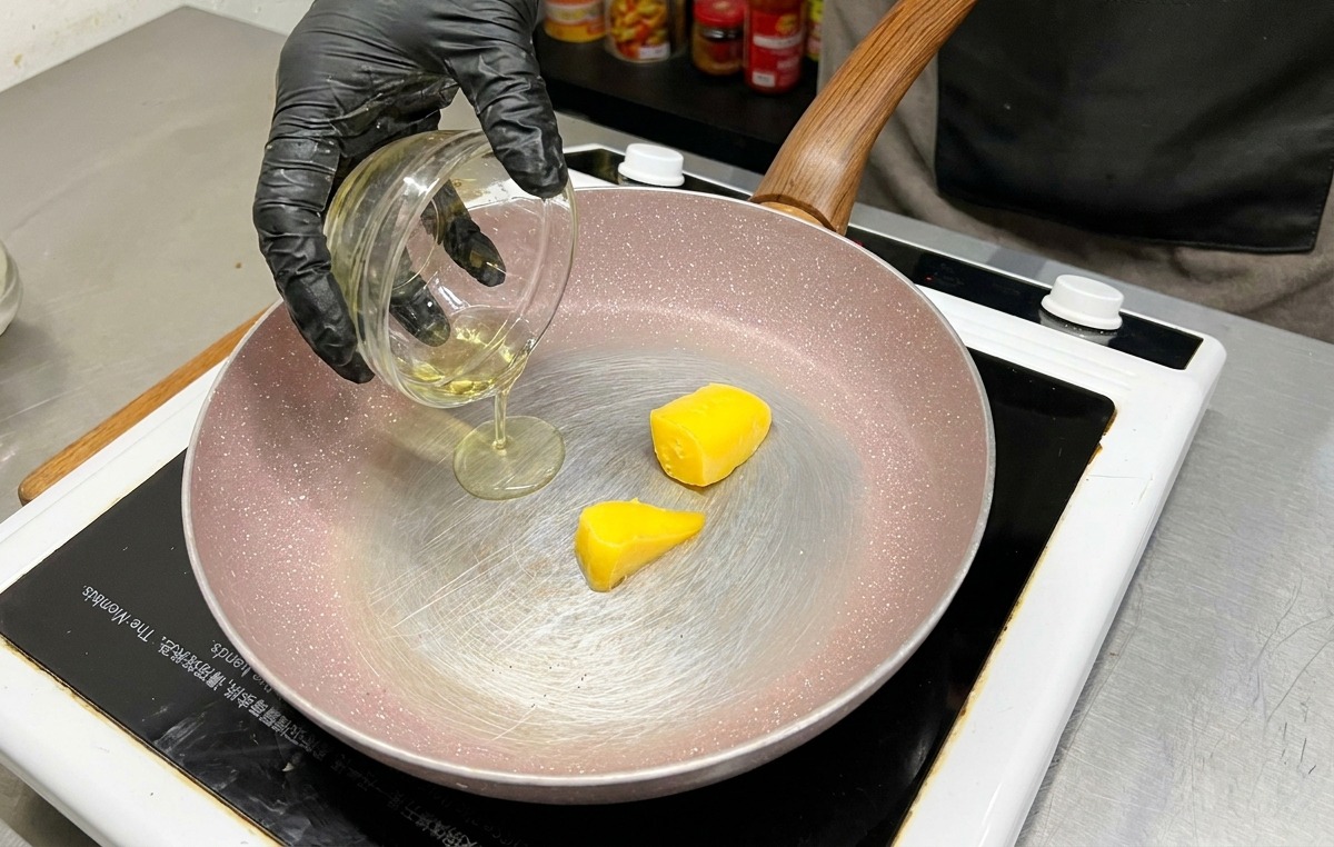 フライパンの中で溶け始めた黄色いバターに、ガラスの器からオリーブオイルが注がれている様子