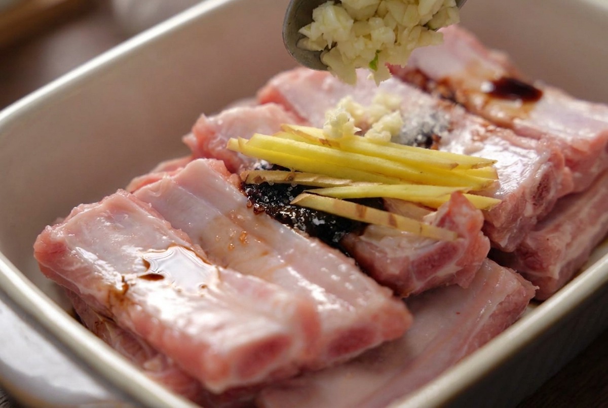 細切りの生姜がのった味付け済みの豚スペアリブに、スプーンでみじん切りのにんにくを加える様子