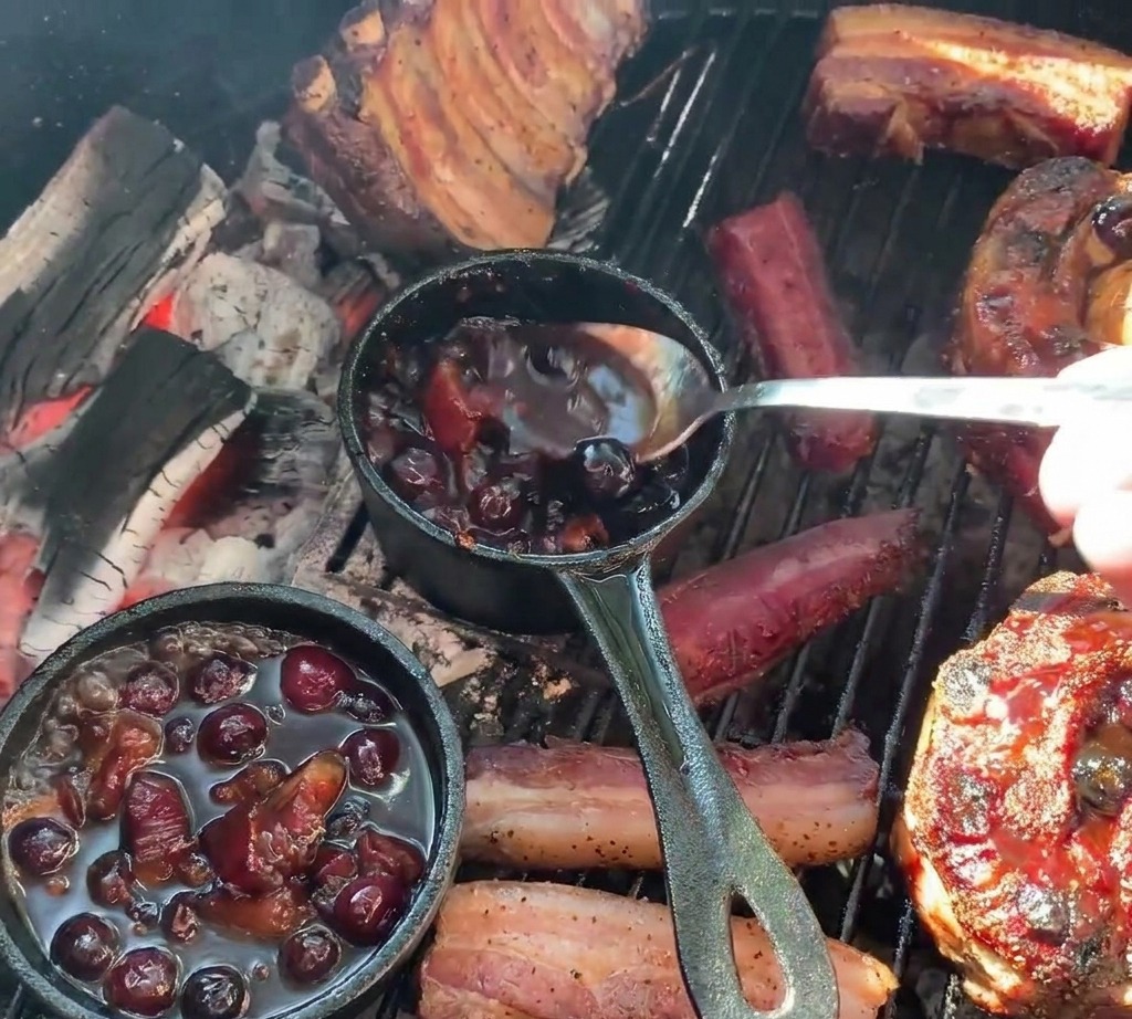 小さな鋳鉄製の鍋から、ポテトが詰まった焼き立てのリブカップへ、スプーンを使って濃いブルーベリーソースをたっぷりとかけている様子。