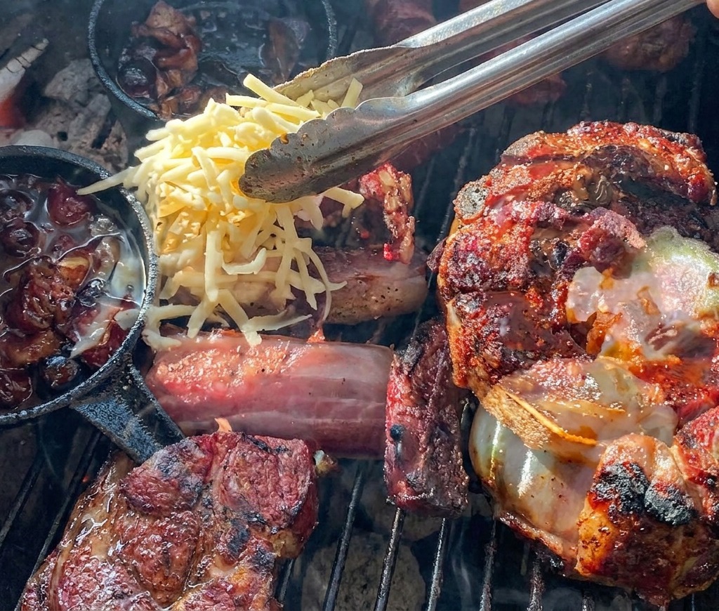 トングを使い、ポテトとブルーベリーソースが詰まったグリルの上の肉カップに、黄色と白の細切りチーズを乗せている様子。