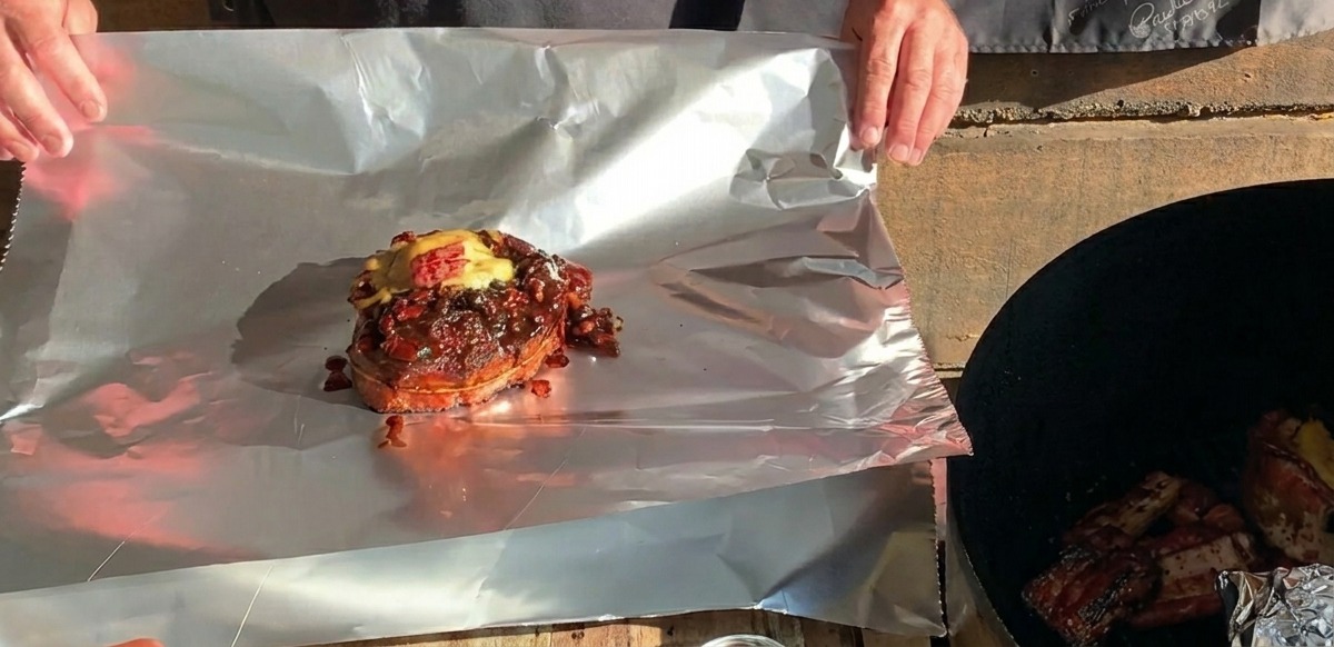 大きめのアルミホイルのシートの上に置かれた、とろけるチーズがのった完成したBBQリブカップ。