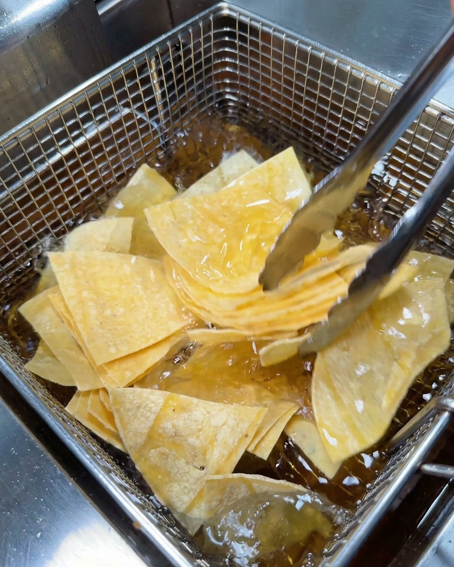 金属製のトングを使って、三角形に切ったトルティーヤをフライヤーの網かごに入れている様子。