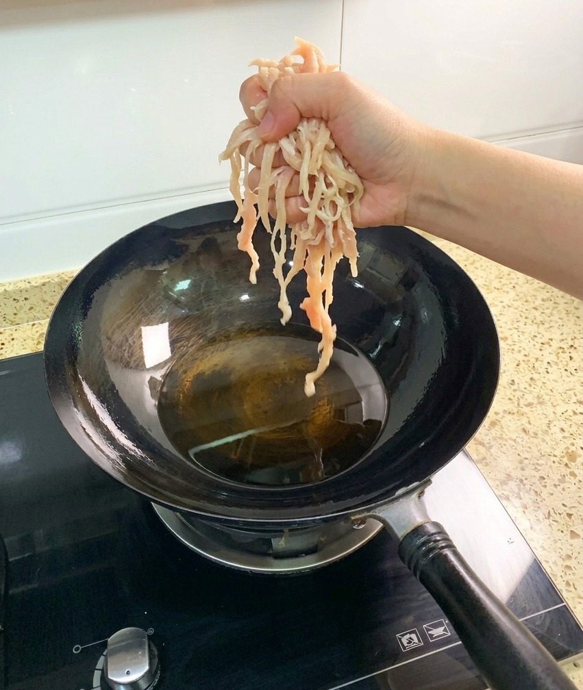 熱した中華鍋の油の中に、千切りにした生の鶏胸肉を入れる様子。