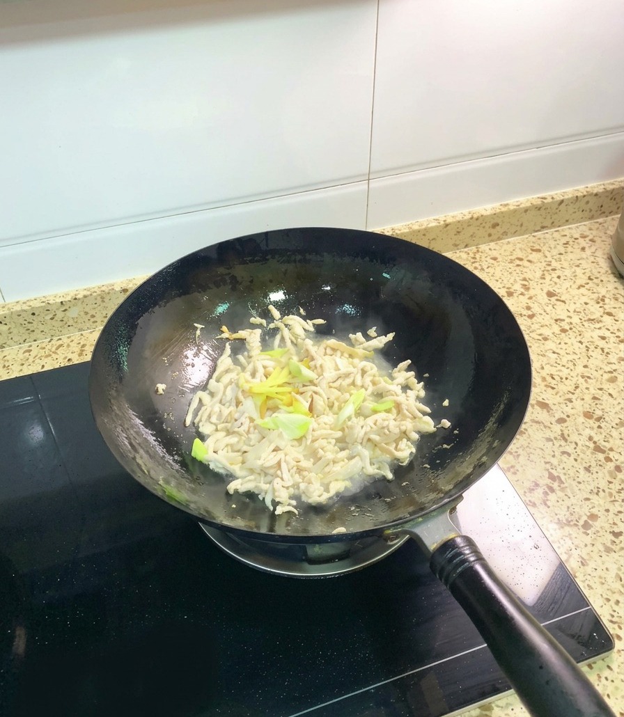中華鍋の中で、少し火が通った鶏肉の千切りと、長ねぎ、スライスした生姜を炒め合わせている様子。