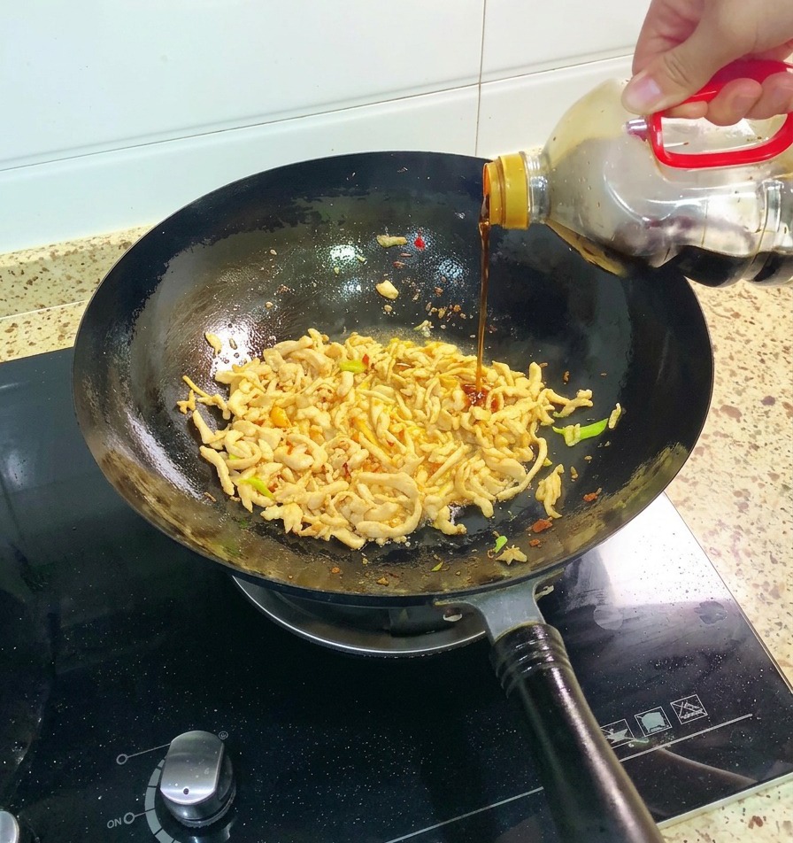 炒めた鶏肉と野菜が入った中華鍋に、ボトルから老抽(中国たまり醤油)を注ぎ入れる様子。