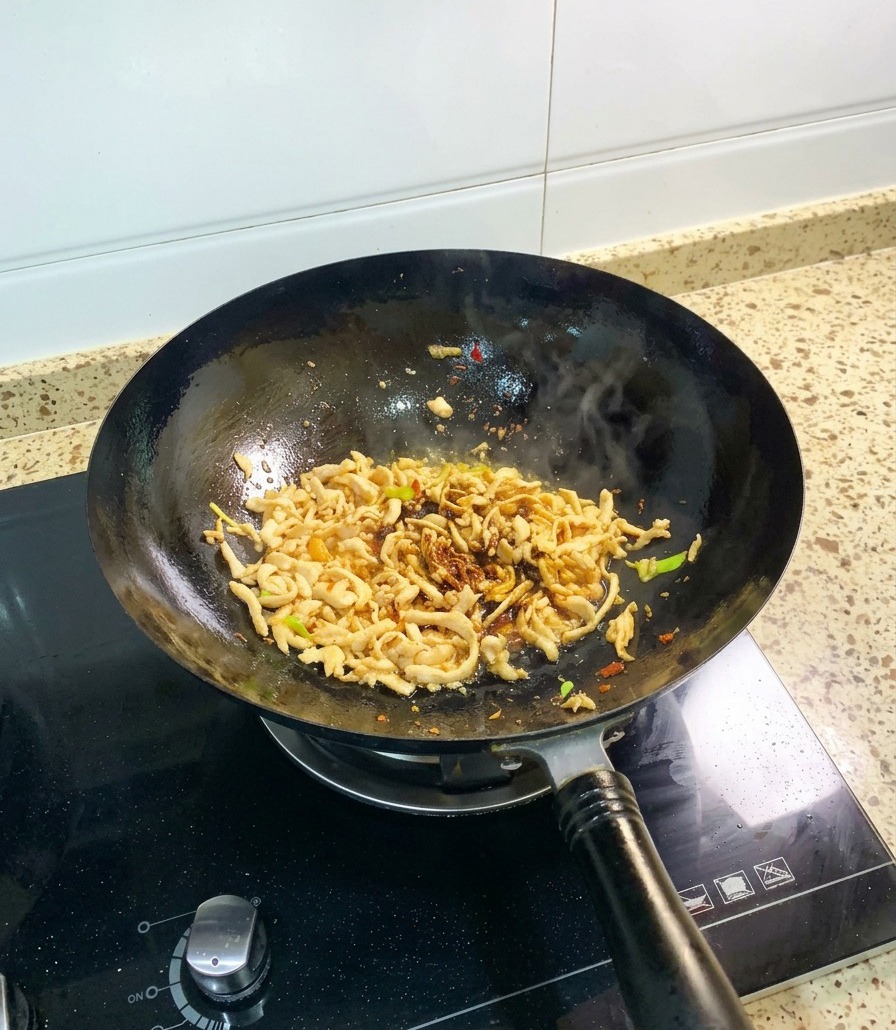黒い中華鍋の中で、たまり醤油を絡めた鶏肉に、とろみのあるオイスターソースを加えて炒めている様子。